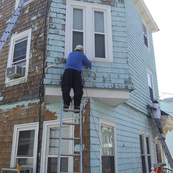 Painter scraping old paint off cedar shingles